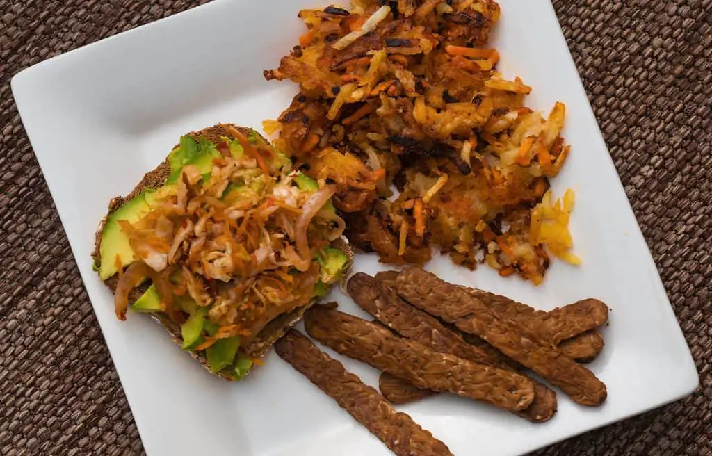 Plant-based vegan breakfast food: avocado toast with kimchi, bacon-flavored tempeh, and root vegetable hashbrowns.